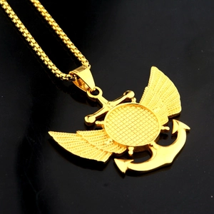 Détail d'un pendentif ancre et ailes dorées avec chaîne box sur surface réfléchissante