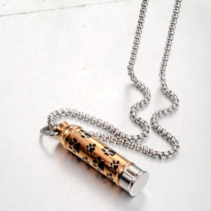 Detailed macro view of a cylindrical gold and silver cremation urn pendant with paw prints