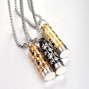 Detailed close-up of three cylindrical paw print cremation pendants in gold black and rose gold