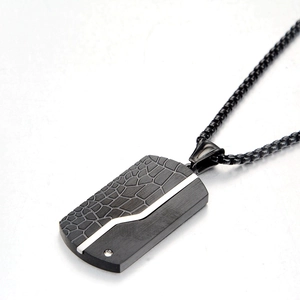 Close-up of black military tag pendant with crocodile texture and brushed steel finish