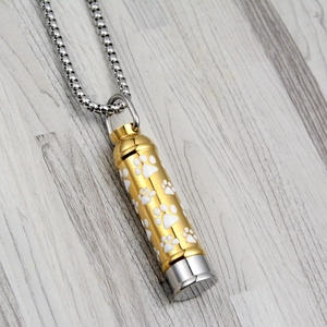 Golden pet cremation urn necklace with paw print patterns and a silver box chain