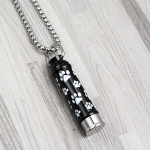 Black stainless steel cylinder pet cremation necklace with white paw prints on wood base