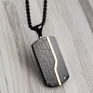 Detail of matte black dog tag pendant with gold accents and crocodile texture
