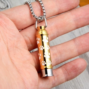Close-up of golden cylindrical pet urn pendant with white paw prints on chunky metal chain