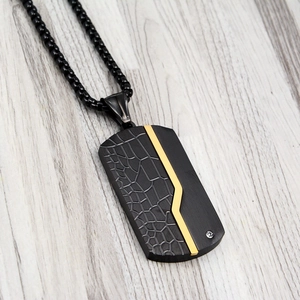Macro detail of black titanium dog tag pendant with gold accent and crocodile texture