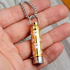 Detail of gold and silver pet urn pendant with white paw print held in palm