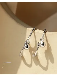 Detail of silver bead drop earring hanging on ceramic bowl edge with soft shadows
