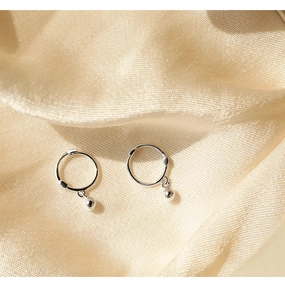 Macro view of minimalist silver hoop earrings with polished bead charms on silk texture
