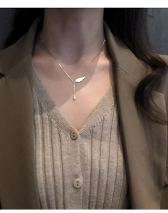 Détail d'un collier aile d'ange doré avec pendentif goutte porté par un mannequin