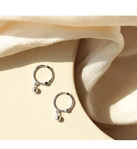 Close-up of minimalist silver hoop earrings with polished ball charms on a beige fabric