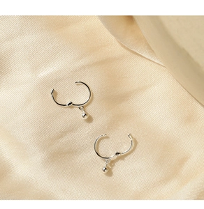 Detailed macro view of minimalist silver ball drop hoop earrings on silk fabric