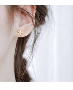 Gros plan d'un mini clou d'oreille étoile dorée avec zircons blancs sur le lobe d'oreille