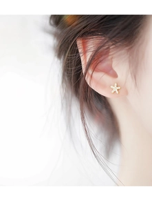 Gros plan d'une boucle d'oreille flocon dorée sertie de cristaux portée par un mannequin