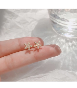 Gros plan de boucles d'oreilles étoile de mer dorées avec strass blancs sur les doigts