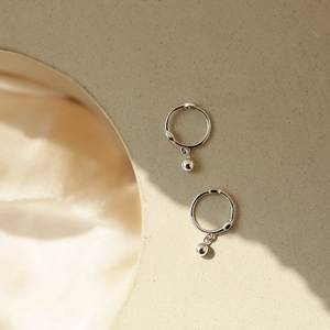 Minimalist silver hoop earrings with small round beads on a warm aesthetic background