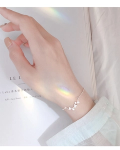 Detail of s925 silver ginkgo leaf bracelet on model wrist with soft rainbow lighting