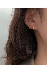 Close-up of minimalist gold plated spiral earrings with small sphere ends worn by model