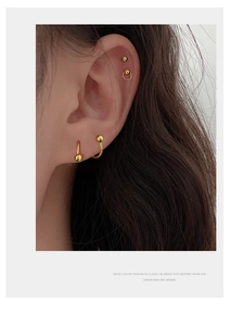 Detailed close-up of minimal golden bead stud and hoop earrings on a female model's ear