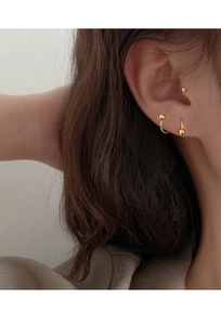 Close-up of minimalist gold helix and lobe stud earrings on a model’s ear