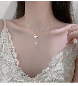 Détail du collier pendentif plume argentée avec de longs glands sur robe en dentelle