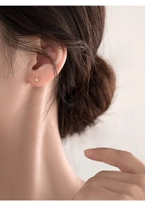 Close-up of small golden flower stud earring with zircon on a female model's ear