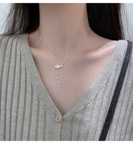 Détail du collier à pendentif plume argentée avec breloques goutte d'eau sur un pull gris