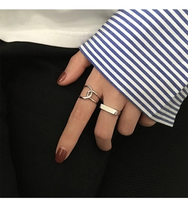 Detail showing a wide silver band and interlaced ring set on finger against a striped shirt