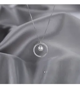 Macro shot of a silver pearl circle pendant on a box chain over grey silk fabric