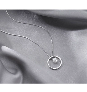 Macro shot of minimalist circle pendant necklace with white pearl on grey silk