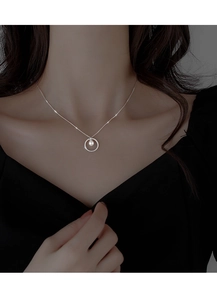 Detail of silver circular pendant with pearl on a model wearing a black outfit