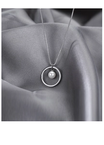 Macro shot of silver circular ring necklace with a hanging white pearl on soft silk background
