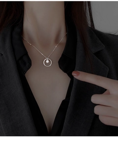 Detail view of a silver circle pendant necklace with a pearl on a model's neck