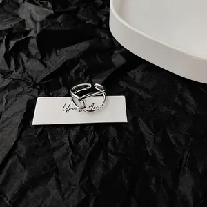 Minimalist silver open ring with hollow interwoven lines on a white ceramic tray