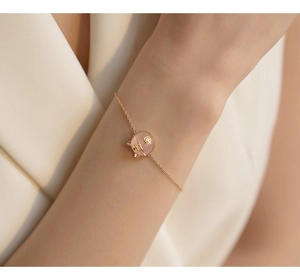 Close-up of elegant gold chain necklace with a pink lucky cat stone pendant on a wrist