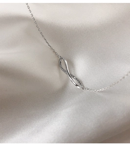 Macro detail of silver infinity pendant with micro-pave crystals on white silk