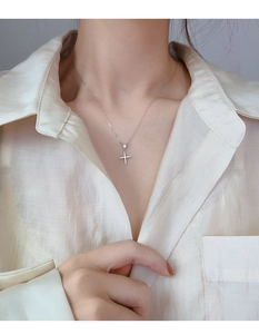 Vue détaillée du collier pendentif croix en argent serti de strass sur un chemisier en soie