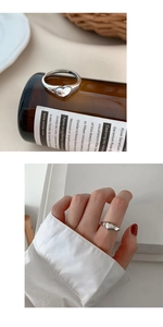 Detail view showing a silver heart ring worn on the index finger with an adjustable band