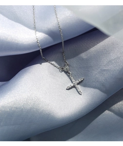 Gros plan d'un pendentif croix argenté serti de zircons sur fond de soie bleue