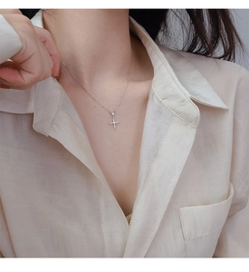 Gros plan d'un pendentif croix en argent avec zircons brillants porté sur une chaîne fine