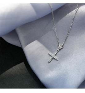 Vue macro d'un collier pendentif croix en argent avec zircons scintillants sur soie bleue