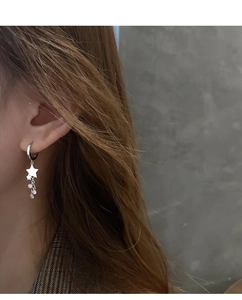 Boucles d'oreilles étoiles en argent avec pampilles portées sur fond gris neutre