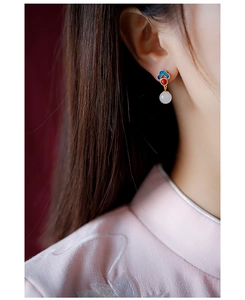 Close-up of vintage Hetian jade earrings with blue enamel cloud patterns and red beads