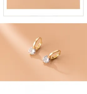 Close-up of gold-plated silver earrings featuring a round zircon stone on a warm beige backdrop