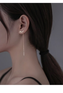 Detail of star tassel drop earrings with long gold chain worn by a model in soft lighting