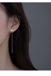Macro close-up of sterling silver star tassel earrings worn on a female ear model