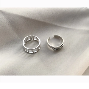 Close-up of S925 sterling silver Roman numeral and smiley face open rings on fabric