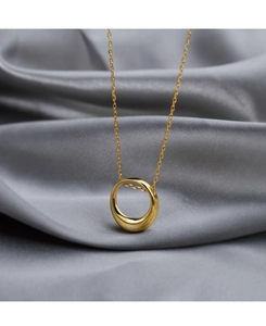 Close-up of golden circular necklace on gray silk background highlighting metallic luster