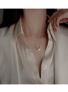 Close-up of minimalist gold circular pendant necklace on woman wearing a silk shirt