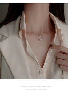Close-up of minimalist silver circular pendant necklace worn with an elegant cream blazer