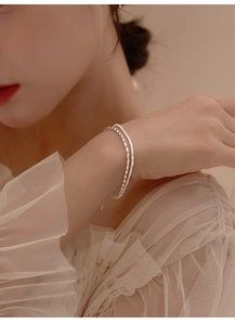 Detail of double-layer silver bead bracelet on model's wrist with lace sleeve